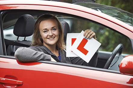 young woman in driving seat of car a holding two learner plates